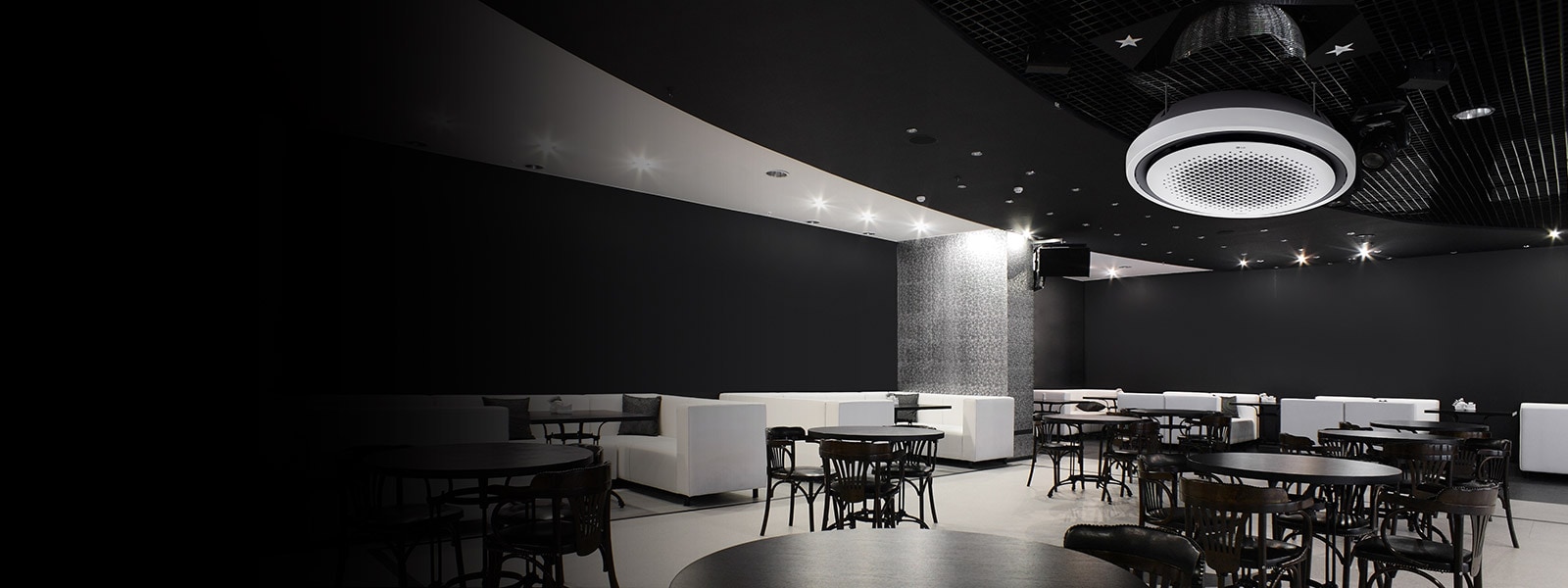 Black and white tone dining area with tables, chairs, and a sofa displayed. LG Round Cassette mounted on the ceiling. 